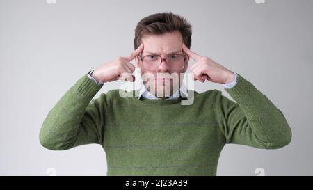 Ein junger lustiger Mann in einer großen Brille hält die Finger an Schläfen und versucht, sich zu erinnern oder eine Idee zu generieren. Studioaufnahme Stockfoto