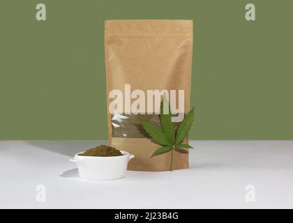 Hanfmehl in einem braunen Kraftpapier Doypack-Beutel mit Lebensmitteln Vorderansicht auf einem grünen Hintergrund. Packungen mit Fenstern für Produkte mit Gewichten. Stockfoto