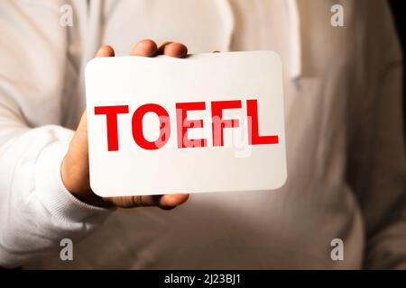 TOEFL - Test of English as a Foreign Language. Text auf weißem Papier auf hellweißem Hintergrund. Im Hintergrund ist eine Lupe, ein Diagramm, eine Kalk Stockfoto