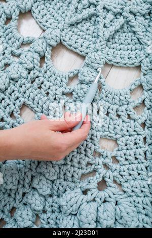 Die Hände der Frauen liegen auf einem Karos aus grober Strickwolle auf einem Holzboden, Draufsicht. Handgefertigter Teppich Stockfoto