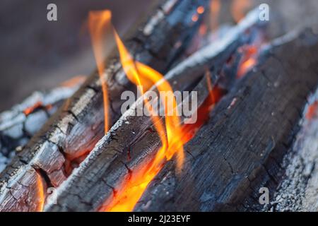 Feuerholz brennt im Kamin in den Flammen eines warmen roten Feuers auf dunklem Hintergrund. Briketts leuchten und brennen, Nahaufnahme. Stockfoto