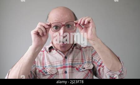 Überrascht stattlichen älteren Mann durch die Brille auf schockierend Inhalt und lachen. Studioaufnahme Stockfoto