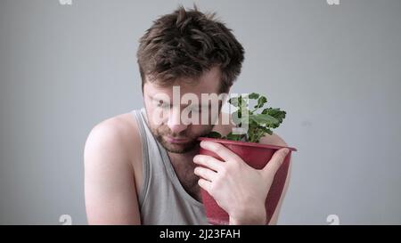 Betrunkener gestresster Mann, der einen Topf umarmt und die Blume allein ist. Konzept von Alkoholismus und schwerem Trinken. Stockfoto