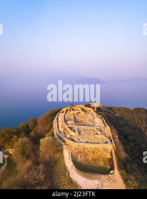 Luftaufnahme der Festung mit einem Kreuz auf einem Hügel im Hintergrund Gardasee. Panorama auf die rocca di manerba von oben. Stockfoto