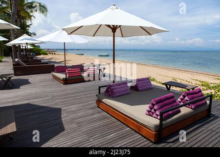 Sonnenliegen, Tische, Stühle am Strand im Griya Santrian Hotel in Sanur, Bali, Indonesien. Stockfoto