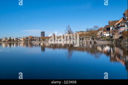 Zug, Schweiz - 31. Dezember 2021: Schöner Blick auf neue und alte Gebäude in der Stadt Zug mit Spiegelungen im Wasser Stockfoto