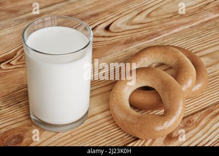 Ein Glas frische Milch und drei Bagels auf einem Holztisch. Stockfoto