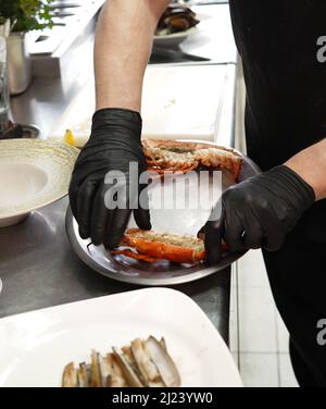 Professioneller Koch, der einen Hummer verarbeitet, um eine Meeresfrüchteplatte zuzubereiten Stockfoto