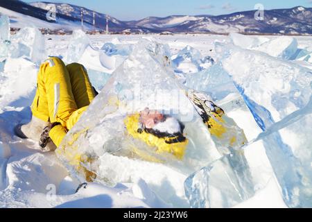 Ein Mädchen im gelben Jumpsuit liegt auf dem Schnee hinter einer Eisscholle Stockfoto