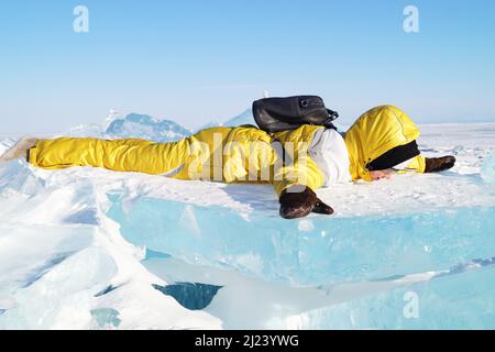 Ein Teenager-Mädchen in einem gelben Jumpsuit liegt auf einer Eisscholle Stockfoto