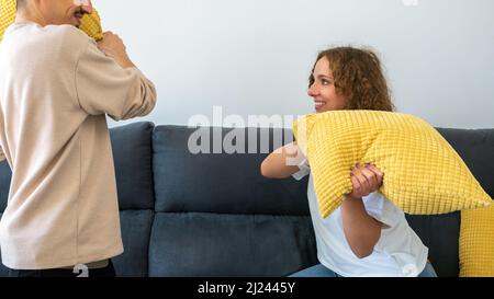 Ein paar von zwei glücklichen Freunden, die Spaß haben, zusammen auf dem Sofa zu Hause zu spielen und mit Kissen zu kämpfen genießen. Die Kissen waren morgens drinnen Stockfoto