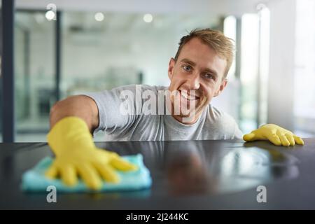 Ziemlich sauber, richtig. Porträt eines jungen Mannes, der in einem Büro die Oberflächen abwischt. Stockfoto