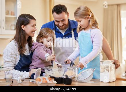 Familienzeit ist alles, was zählt. Aufnahme einer Familie, die zusammen bäckt, während ein kleines Mädchen eine Schüssel mit Kuchenteig rührt. Stockfoto