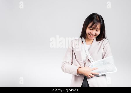 Arm gebrochen. Geschäftsfrau zuversichtlich lächelnd gebrochenen Arm nach Unfall und tragen Armschiene für die Behandlung, aufgeregt glücklich asiatische weibliche Sling Unterstützung han Stockfoto
