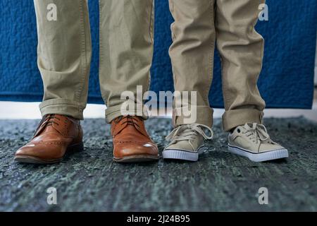 Eines Tages füllt er Daddys Schuhe aus. Ausgeschnittene Aufnahme eines nicht erkennbaren Mannes und seines Sohnes, der nebeneinander steht. Stockfoto