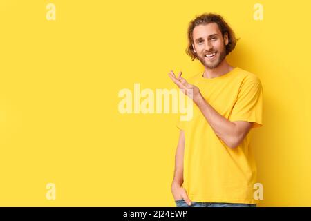 Hübscher junger Mann im stylischen T-Shirt mit etwas auf gelbem Hintergrund Stockfoto