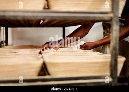 Ich werde meine erste Charge für den Ofen vorbereiten. Zugeschnittenes Bild eines männlichen Bäckers, der den Teig auf einen Backwagen legt. Stockfoto