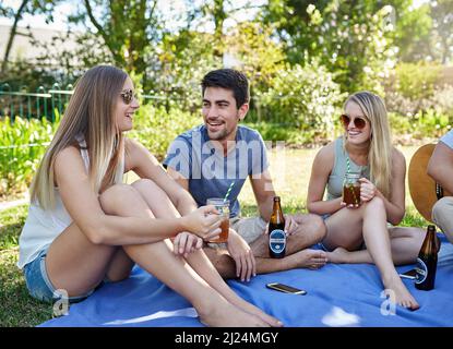 Mit Freunden chillen. Eine kleine Aufnahme einer jungen Gruppe von Freunden, die in der Sommersonne ein paar Drinks genießen. Stockfoto