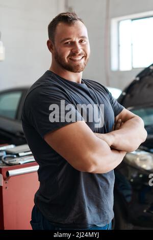 Ich habe dein Auto wieder wie neu laufen lassen. Aufnahme eines Mechanikers, der mit gekreuzten Armen in einer Autowerkstatt posiert. Stockfoto