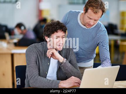 Große Köpfe denken gleich. Aufnahme von zwei Kollegen, die in einer legeren Arbeitsumgebung zusammen an einem Laptop arbeiten. Stockfoto