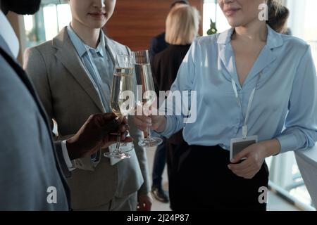 Drei junge erfolgreiche Makler in formalwear, die mit Champagner-Flöten am Buffet im Restaurant des Business Centers klirren Stockfoto