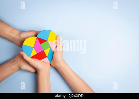 Konzept des Welt-Autismus-Tages. Erwachsene und Kinder Hände halten Puzzle Herz auf hellblauem Hintergrund. Draufsicht Stockfoto