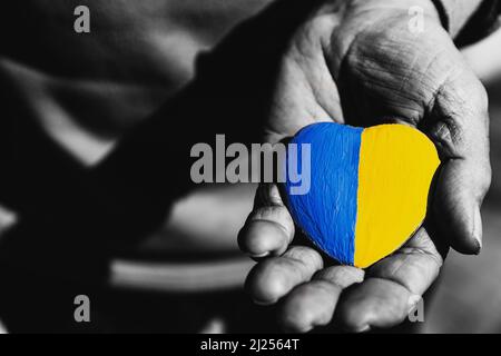 Ältere Mann oder Soldat Hände halten herzförmigen Stein mit Ukraine Nationalflagge Farben gemalt. Betet für die Ukraine, beendet den Krieg, rettet die Ukraine und ihre Kinder. Keine Invasion, Besetzung und Terrorismus Stockfoto