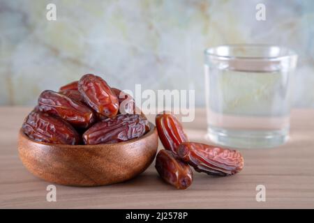 Glas Wasser mit einer Schale Datteln Obst auf einem hölzernen Hintergrund.Muslime brechen das Fasten mit Wasser und Datteln Stockfoto
