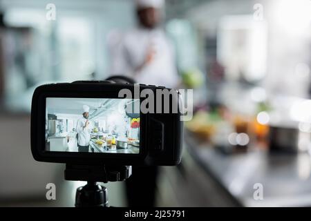 Nahaufnahme Kamera Aufnahme Gastronomie Experte in Restaurant Küche Filmen kulinarischen Kurs beim Kochen leckeres Gericht. Chefkoch vlogging Vorbereitung von Gourmet-Essen für gastronomische Kurs im Internet. Stockfoto