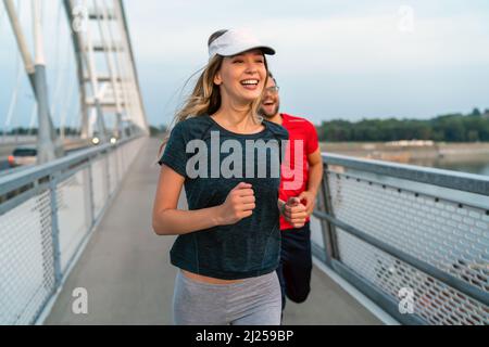 Workout am frühen Morgen. Glückliches Paar, das über die Brücke läuft. Ein gesunder Lebensstil. Stockfoto
