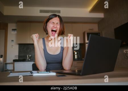 Remote-Job, Ausfall und Stress-Konzept - wütende junge Frau mit Laptop-Computer arbeiten zu Hause im Büro. Schreien mit aggressivem Ausdruck und Arme angehoben. Frustration Konzept. Stockfoto