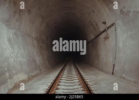 Die Eisenbahnstrecke führt in den dunklen Tunneleingang des Zuges. Reisen mit dem Zug, Raum für Text, selektiver Fokus. Stockfoto