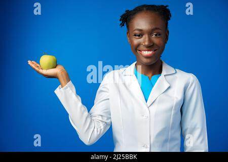 Schöne afrikanische Frau, die im blauen Studio Apfel in der Hand hält Stockfoto