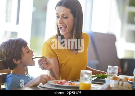 Ich muss das Gemüse essen. Eine kurze Aufnahme einer Mutter und ihres kleinen Sohnes, die zu Hause gemeinsam essen. Stockfoto