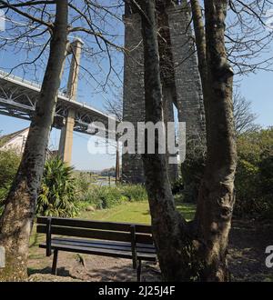 Eine leere Bank in einem abgelegenen Park unter der Royal Albert Bridge in Saltash bietet den Besuchern einen Blick auf den Fluss Tamar und die Hängebrücke Stockfoto