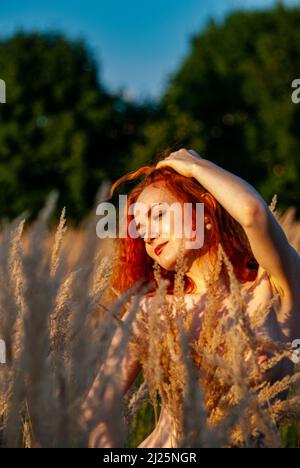 Rothaarige schöne Mädchen sitzt mit ihrem Rücken in schwarzem, langes Kleid im Gras Stockfoto