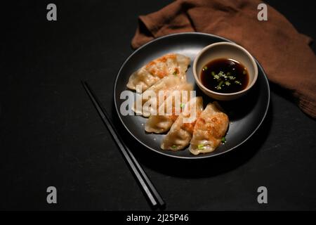 Schwarzer Tischhintergrund mit einem Teller mit einer asiatischen gebratenen Knödel mit süßer Sojasauce. Leckeres asiatisches Speisekonzept. Stockfoto