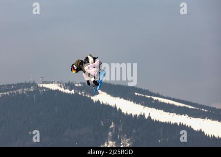 SPINDLERUV MLYN, TSCHECHISCHE REPUBLIK - 18.. März. 2022: Snowboarder springt gegen den blauen Himmel. Snowboarden. Ein junger Snowboarder springt im Spindleruv ml Stockfoto