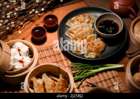 Authentische chinesische Küche mit gebratenem Knödel oder Gyoza, gedünsteten Schweinebraten und heißem Tee auf dem Esstisch. Stockfoto