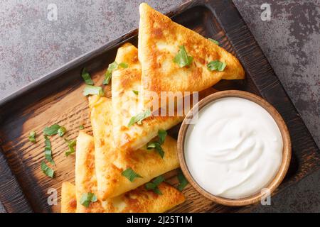 Gebratene dreieckige Pfannkuchen mit Fleisch, serviert mit Sauerrahm aus nächster Nähe auf einem Holztablett auf dem Tisch. Horizontale Draufsicht von oben Stockfoto