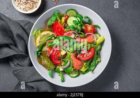 Frischer Salat mit Lachs, Avocado, Gurke und Tomaten auf dunklem Grund. Stockfoto