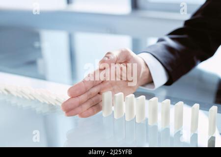 Geschäftsmann Hand Stop Dominos kontinuierlich gestürzt. Nahaufnahme. Stockfoto