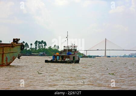 Schlepper mit einem Lastkahn nähern sich der Rạch Miễu-Brücke über den Mekong (Sông Mỹ Tho-Zweig) in der Nähe von Mỹ Tho, Provinz Tiền Giang, Vietnam Stockfoto