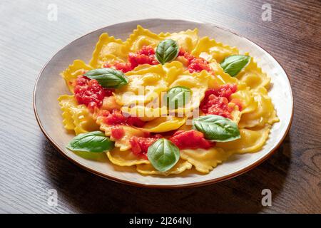 Ravioli mit Tomatensauce und frischen Basilikumblättern, italienisches Rezept, auf einem dunklen rustikalen Holztisch Stockfoto