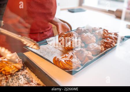 Frische hausgemachte Zimtbrötchen oder Zimtbrötchen sind auf einem Backblech, es gibt eine nicht erkennbare Person trägt eine Schürze im Hintergrund. Stockfoto