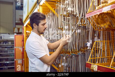 Männlicher Kunde im Regal im Baumarkt wählt Edelstahl-Rohrleitungsschläuche. Stockfoto