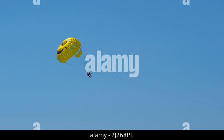 Gelber Fallschirm im blauen Himmel über dem Meer. Parasailing Extremsport am Strand. Stockfoto