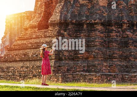 Konzept für Alleinreisende. Glückliche asiatische Frau in rotem Kleid, die Bild der alten Pagode um den historischen Tempel für den Kulturtourismus in Ayutthaya macht Stockfoto