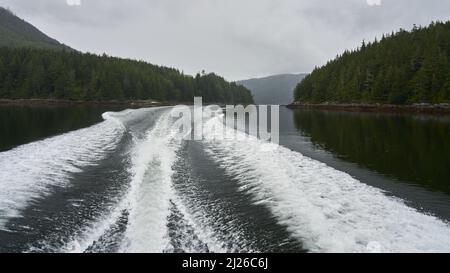 Das weiße Boot wacht am Heck eines Motorbootes auf, das an einem düsteren Frühlingstag mit hoher Geschwindigkeit durch die engen Inselpassagen fährt. Stockfoto