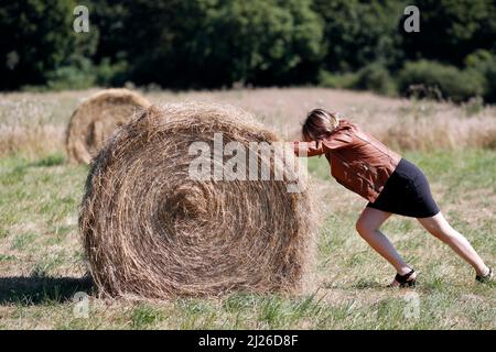 Frau mit einer Rolle Stroh in einem frisch geschnittenen Weizenfeld verpackt. Stockfoto